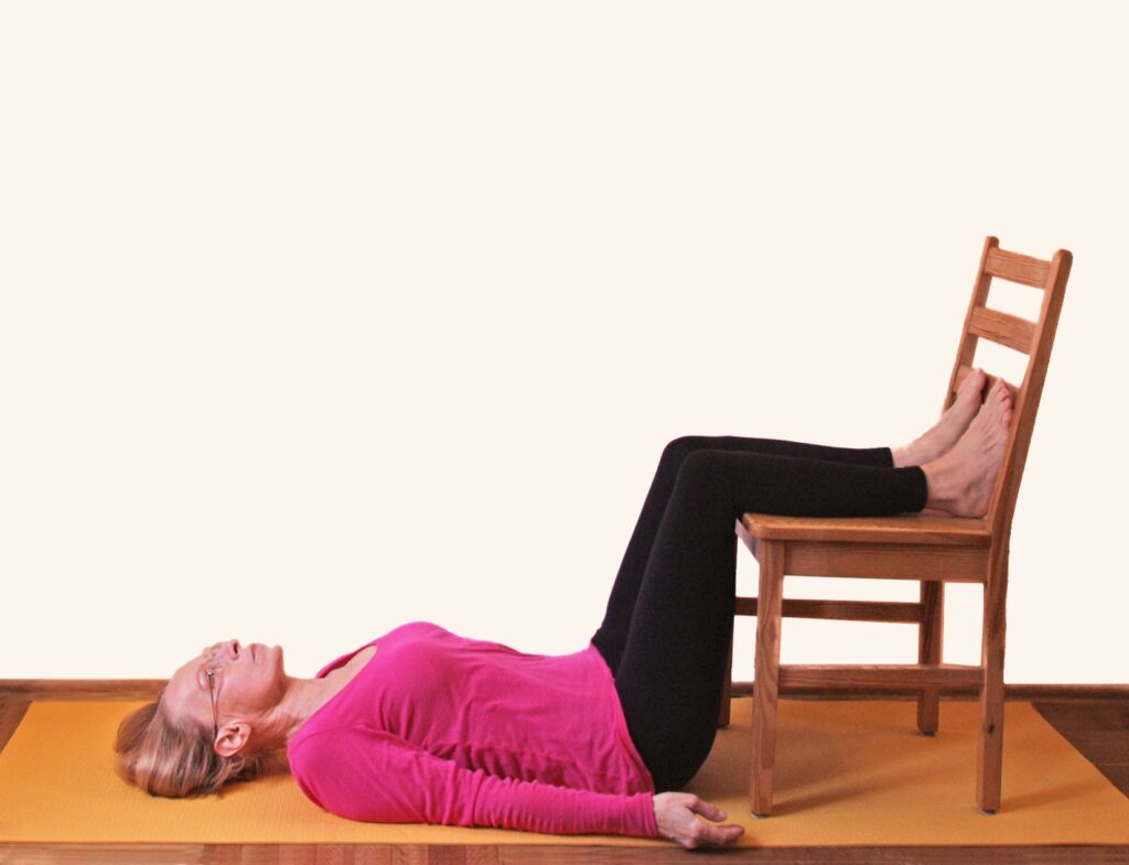 kobieta w siavasanie, pozycji relaksacyjnej jogi na macie, z użyciem krzesła, Joga na bóle pleców i ból kręgosłupa