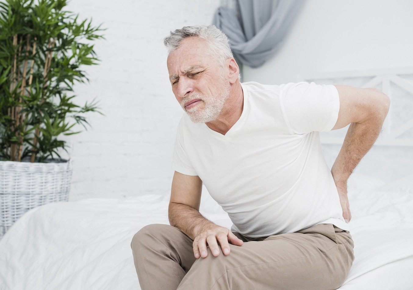 mężczyzna siedzący na łóżku łapie się za bolące plecy